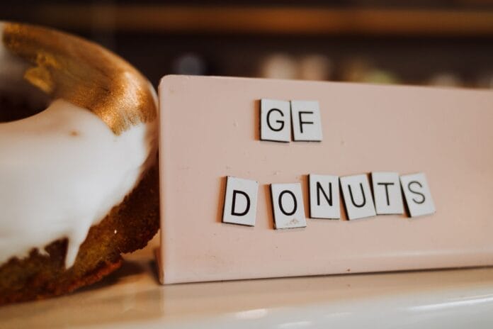 Bezglutenowe donuty z białą polewą i złotymi akcentami na pastelowym tle Bezglutenowe donuty z białą polewą i złotymi akcentami na pastelowym tle