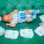 Niemowlę na zielonej kanapie wśród pieluch i kosmetyków do pielęgnacji
